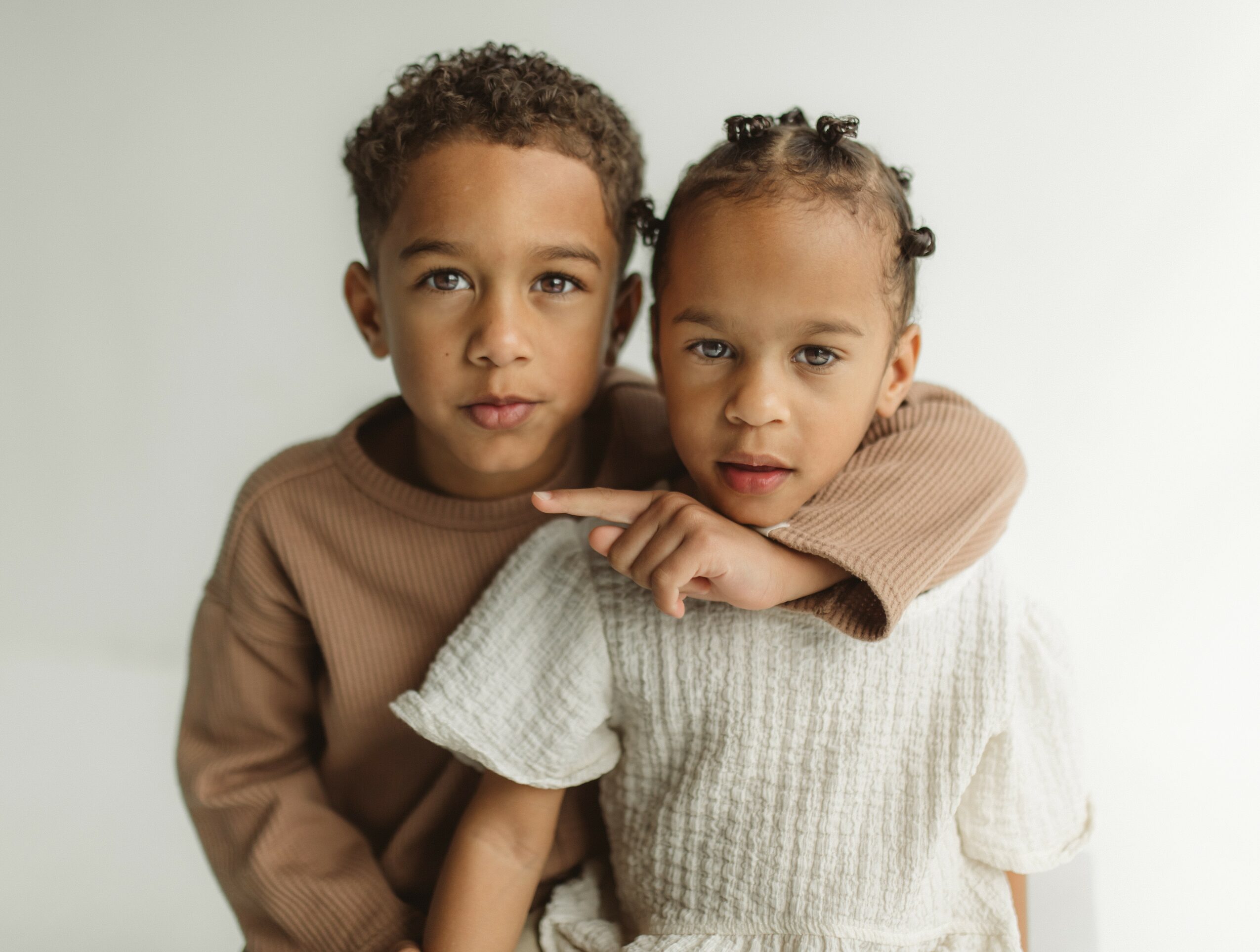 Two children, a boy and a girl, close together, looking at the camera against a plain background.