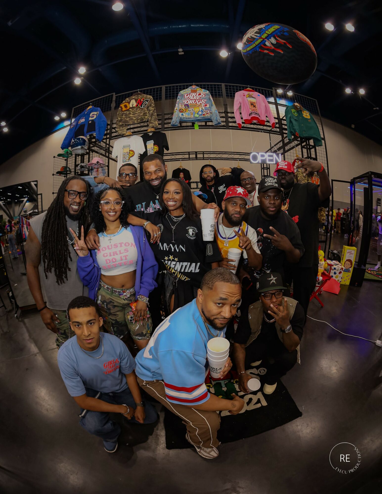 Group of people inside a store with clothing and accessories, some holding drinks, smiling at the camera.