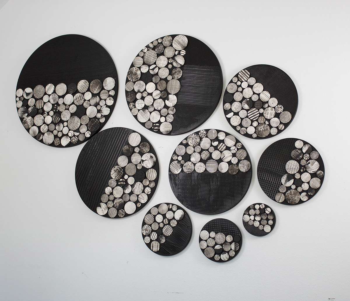 Multiple circular black trays filled with small wooden logs arranged on a white surface.