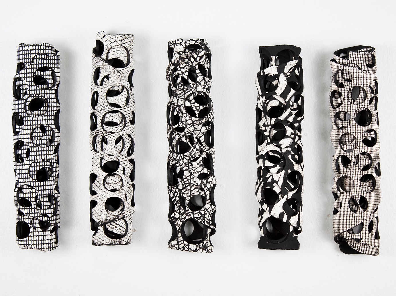 Five cylindrical objects with black and white abstract patterns, arranged in a row against a white background.