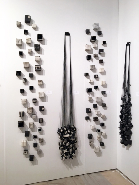 Wall with geometric black and white cube decorations and hanging black objects, arranged vertically, in a gallery setting.