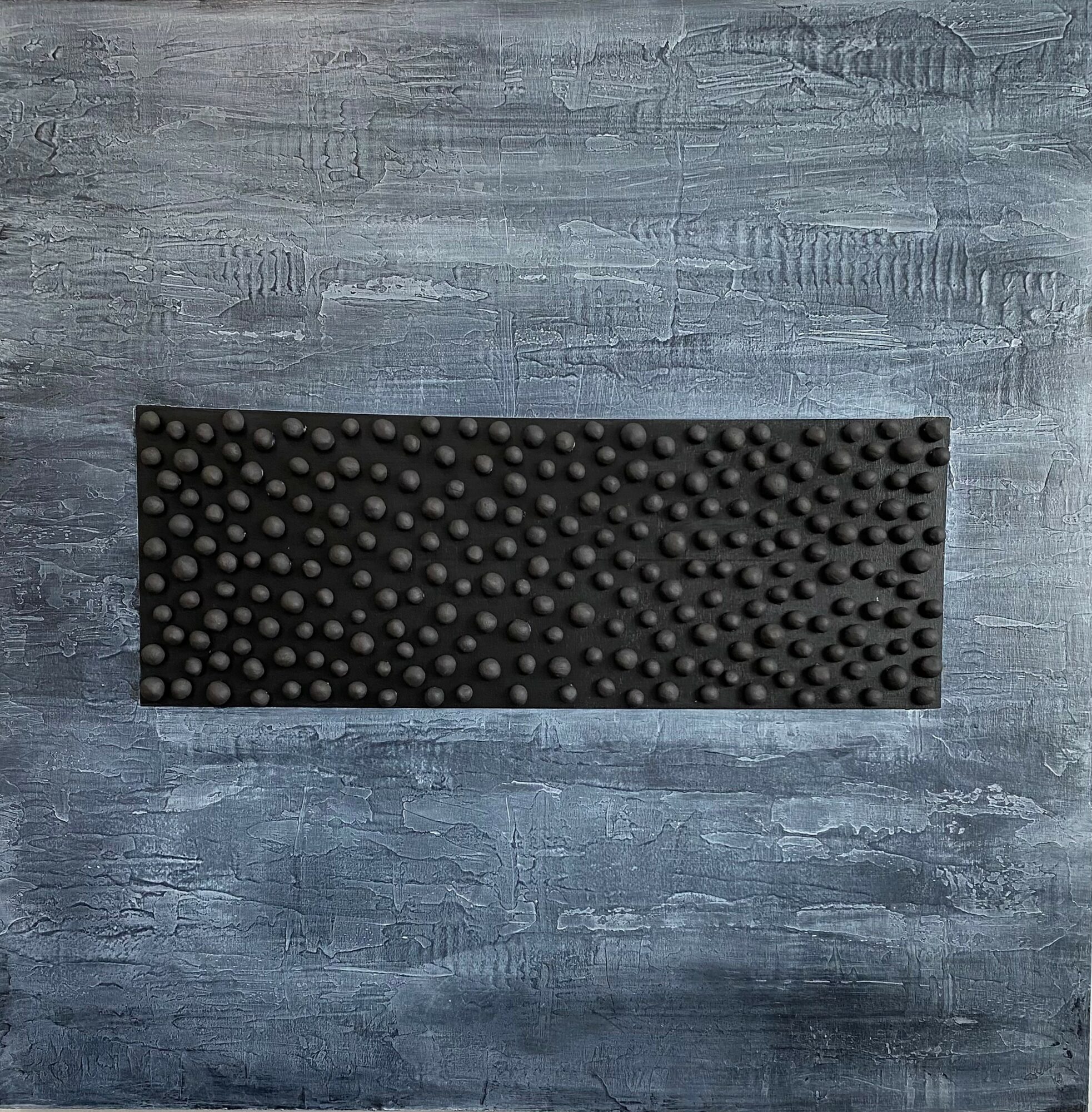 Rectangular black textured mat on a blue-gray wooden surface, with small raised bumps, centered in the image.