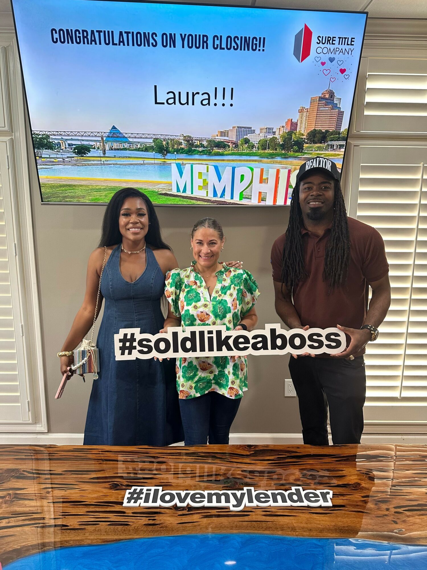 Two women standing indoors, one holding a sign with hashtag #soliddickeboss and a trophy, in front of a large screen.