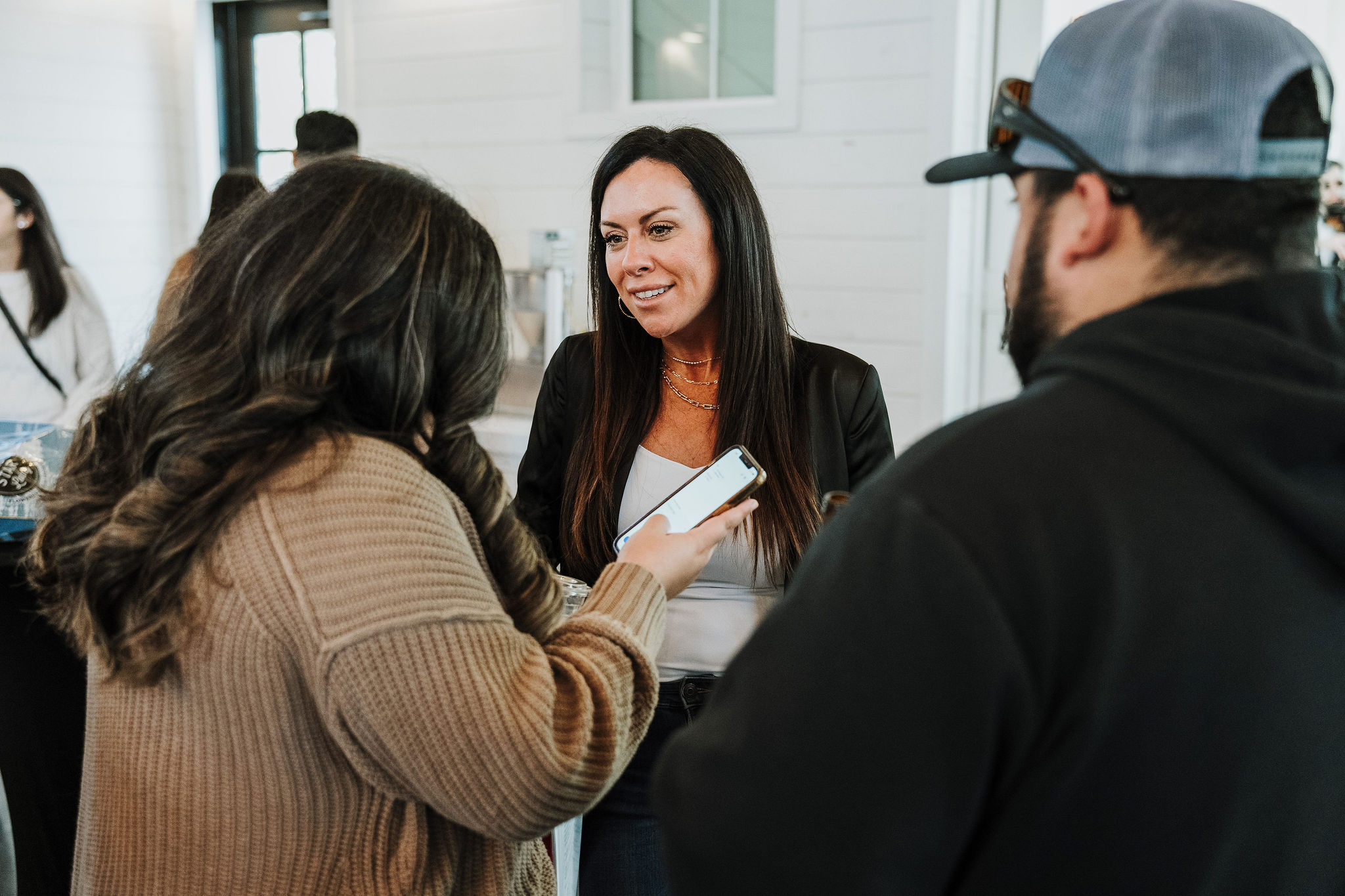 Three people engaged in conversation indoors, woman smiling, holding a notebook, others listening attentively.