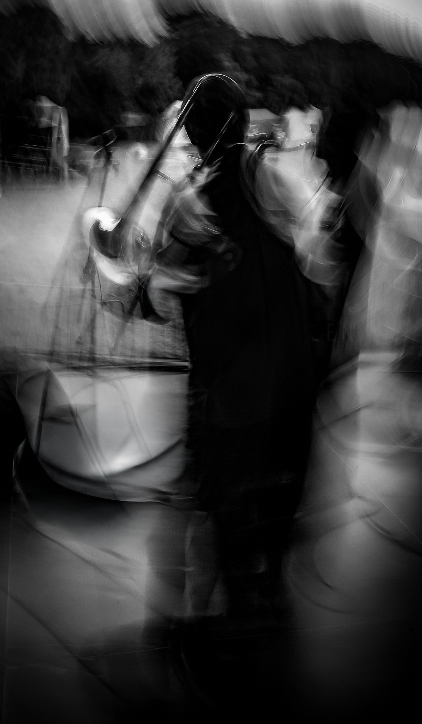 Blurry black and white photo of a person holding a trumpet, with other people in the background.