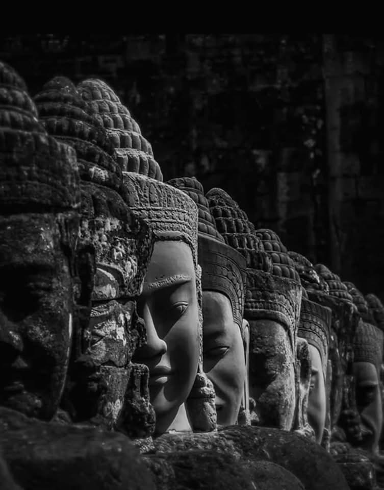Multiple stone carved faces with serene expressions, part of ancient temple ruins, in black and white.