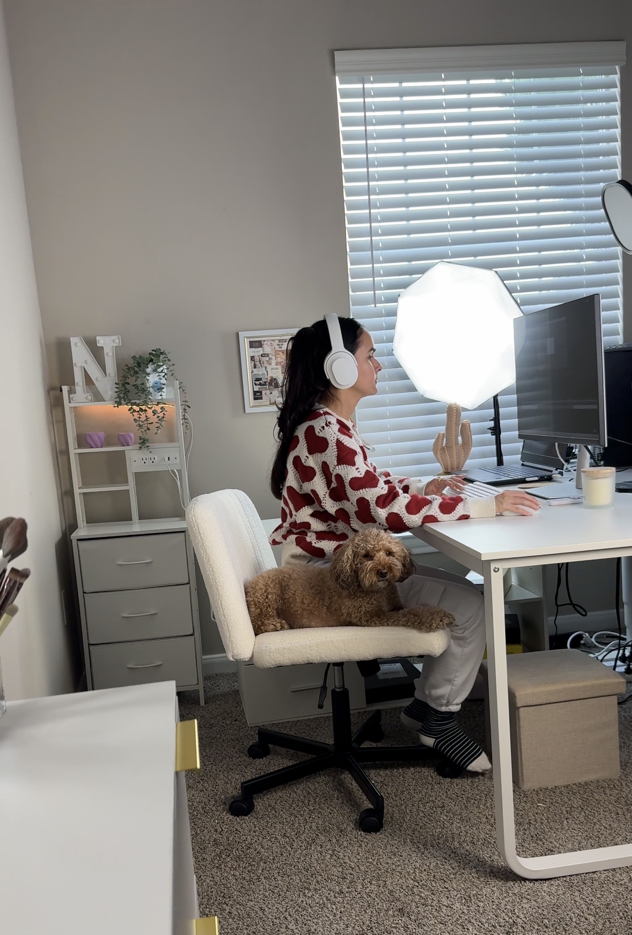 Child with headphones sitting at a desk, holding a light diffuser, with a dog on the chair, in a home office.
