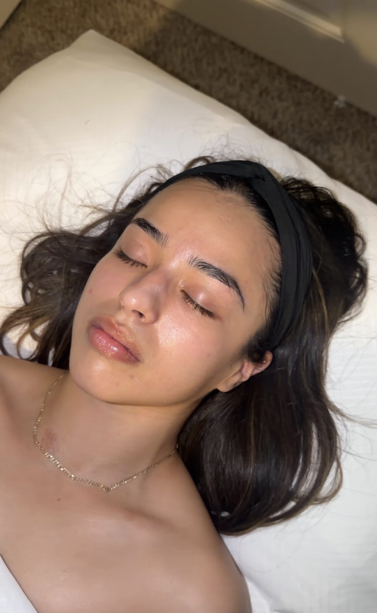 Young woman with dark hair and a headband, lying on a pillow with eyes closed, relaxed expression.
