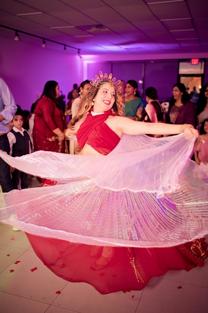 Woman spinning in a pink and red dress at a celebration with people in the background.