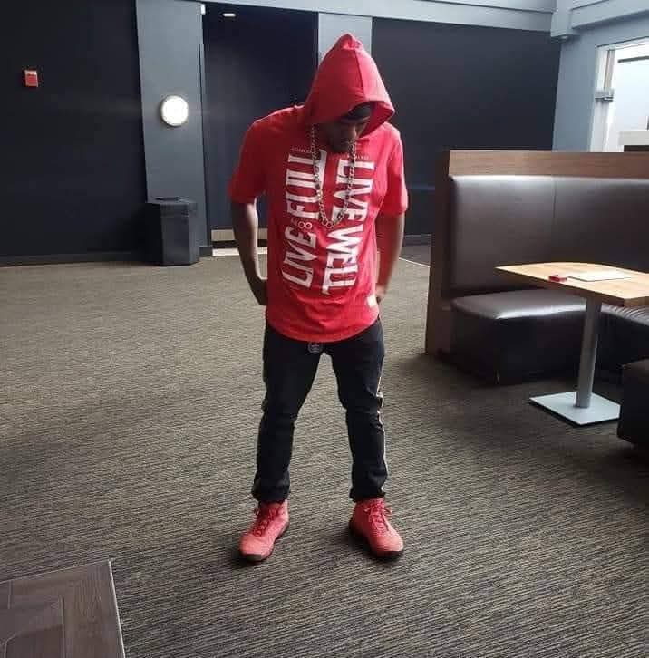 Child in red hoodie and black pants standing indoors, looking down, with booth seating and a window in background.