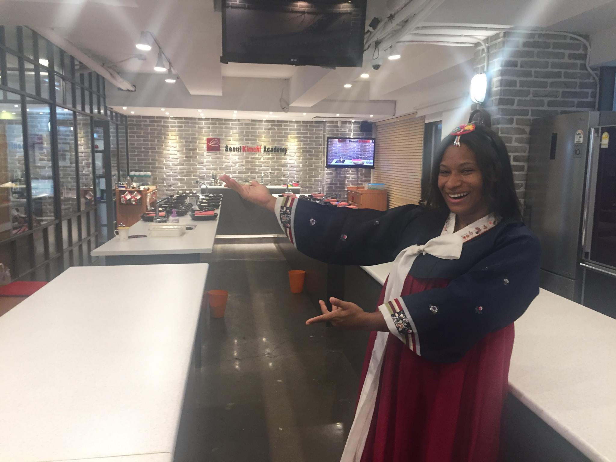 Woman smiling and pointing at a counter in a modern indoor space with brick walls and large windows.