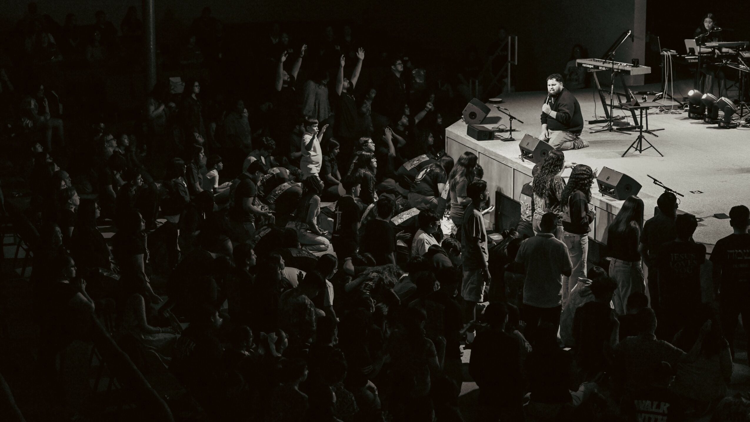 Musician performing on stage with audience watching, in a dark indoor setting.