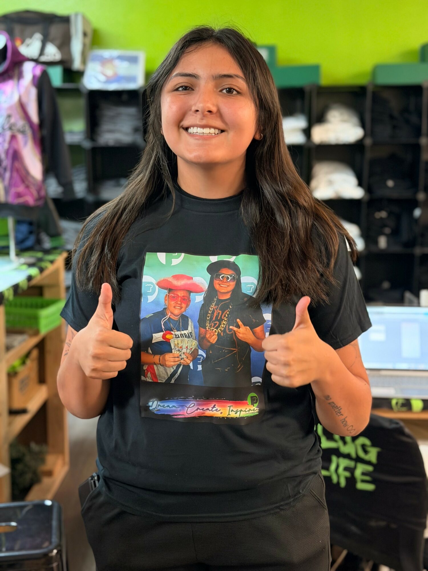 Young woman smiling and giving two thumbs up in a store with shelves and clothing in background.