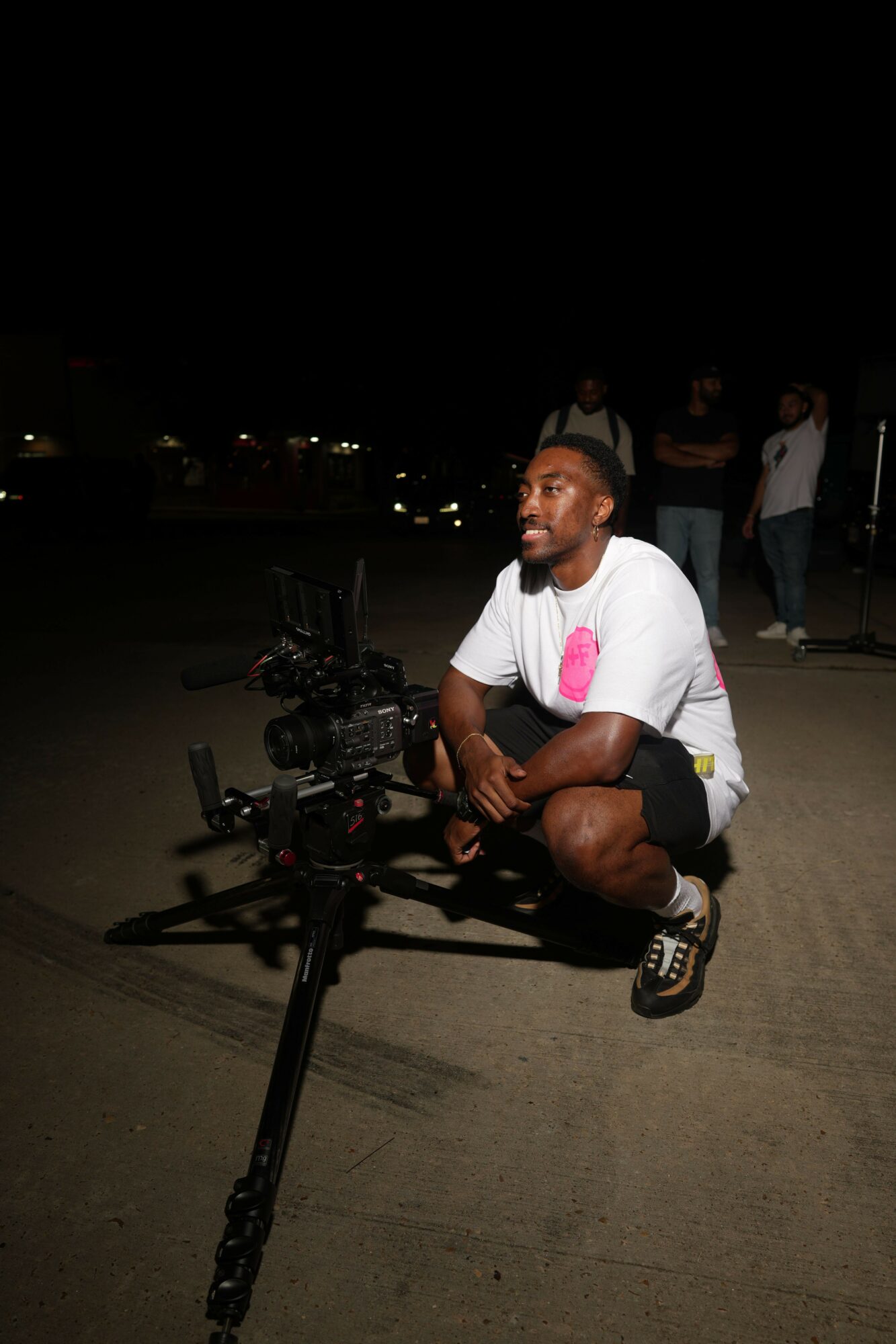 Person sitting on a bicycle at night, wearing a white shirt and black shorts, with a dark background.