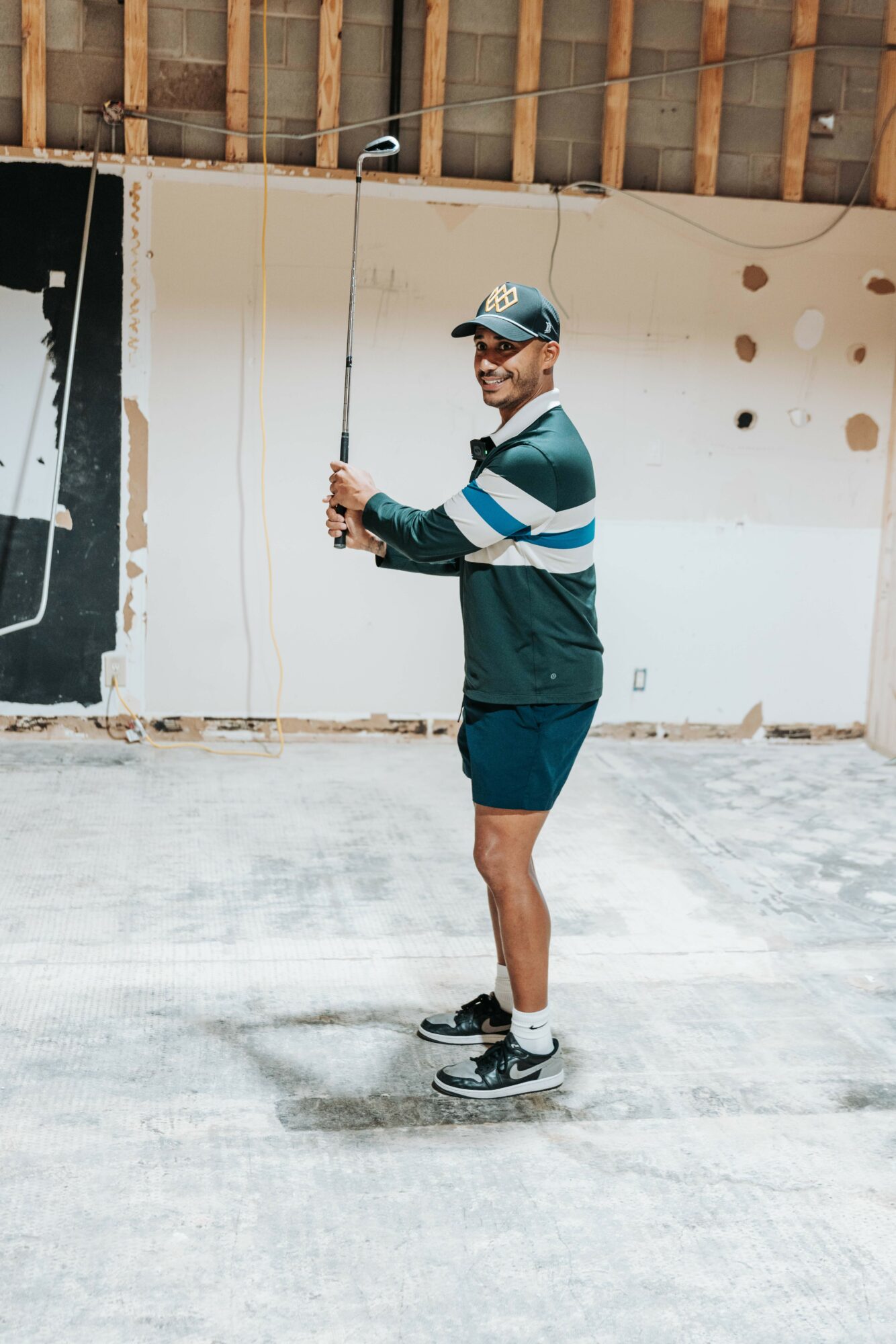 Person standing on skateboard, holding a fishing rod, smiling, in an unfinished indoor space with a concrete floor and wall.