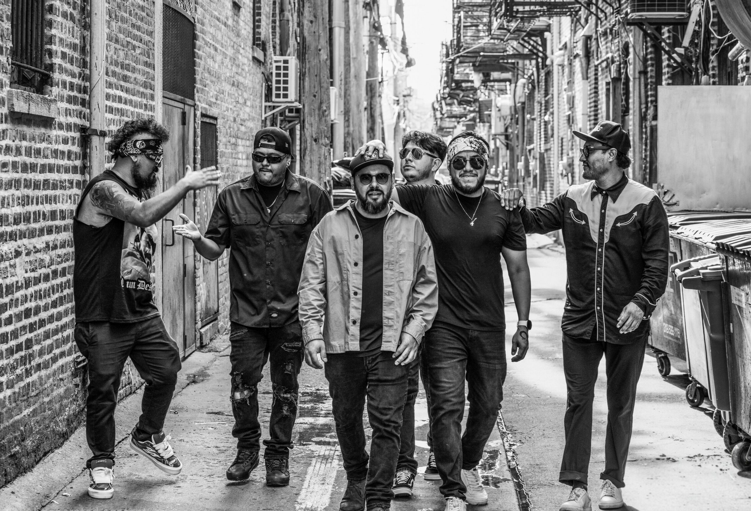 Group of six people walking down a narrow urban alleyway, some wearing sunglasses and casual clothing.