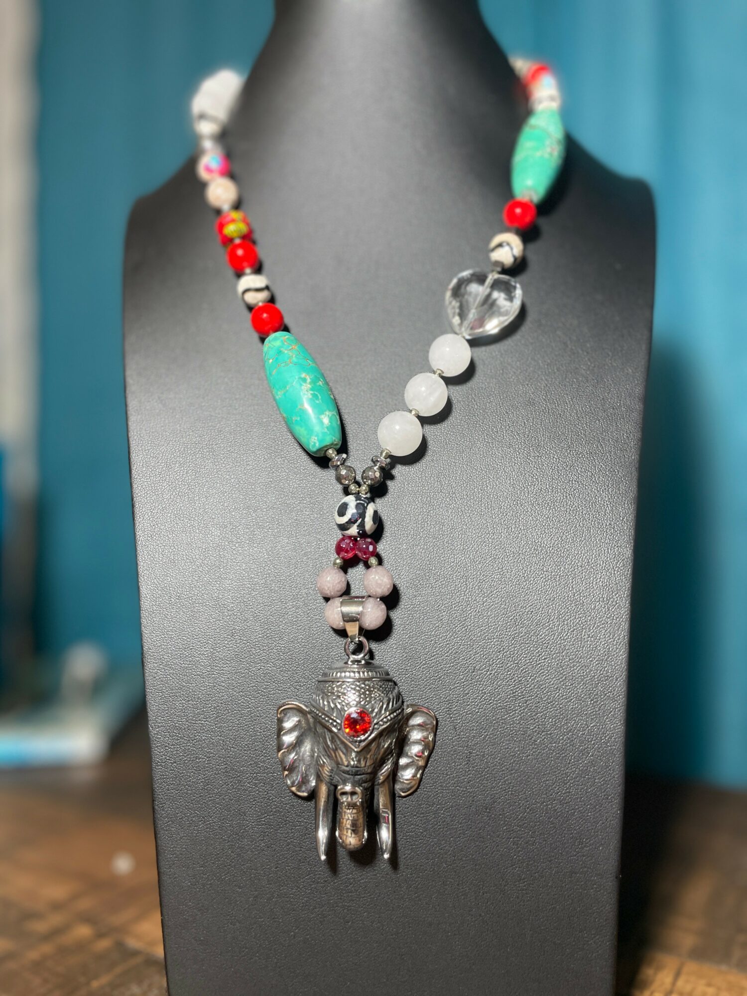 Necklace with colorful beads and a large elephant pendant displayed on a black bust.