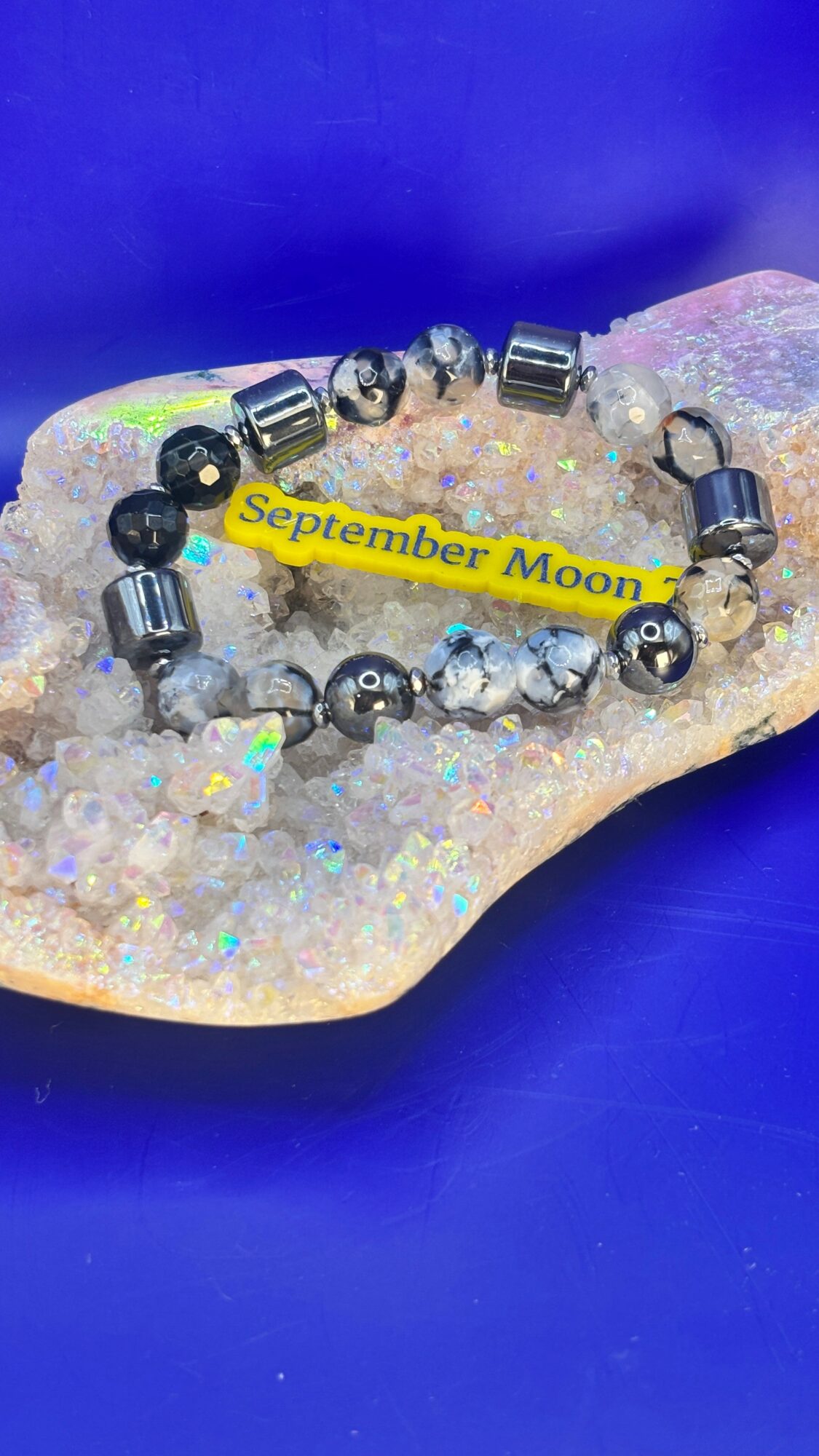 Bracelet with black and silver beads on a glittery surface, with a yellow tag reading 'September Moon'.
