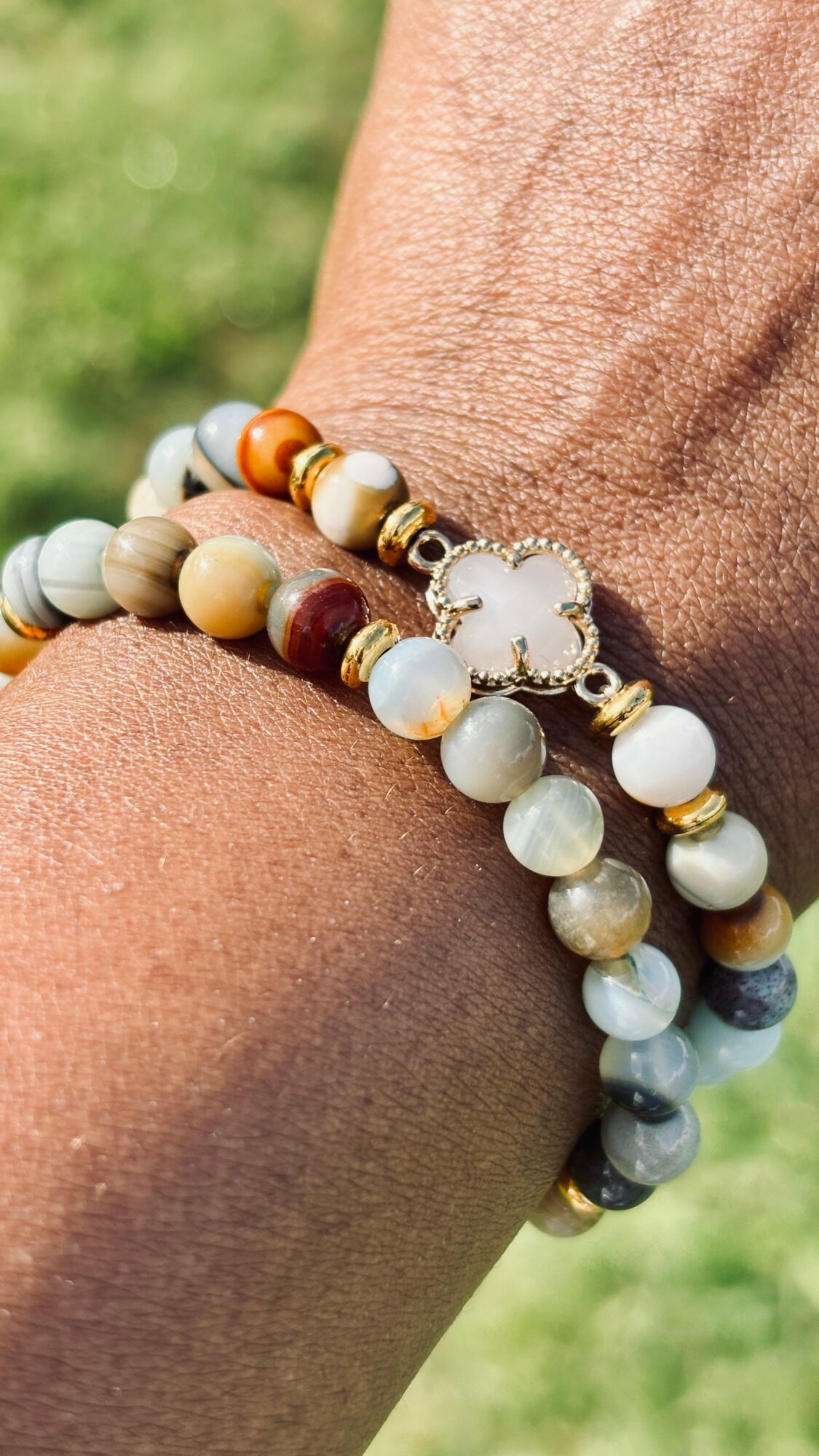 Beaded bracelet with various colored beads and a clover-shaped charm on a person's wrist outdoors.