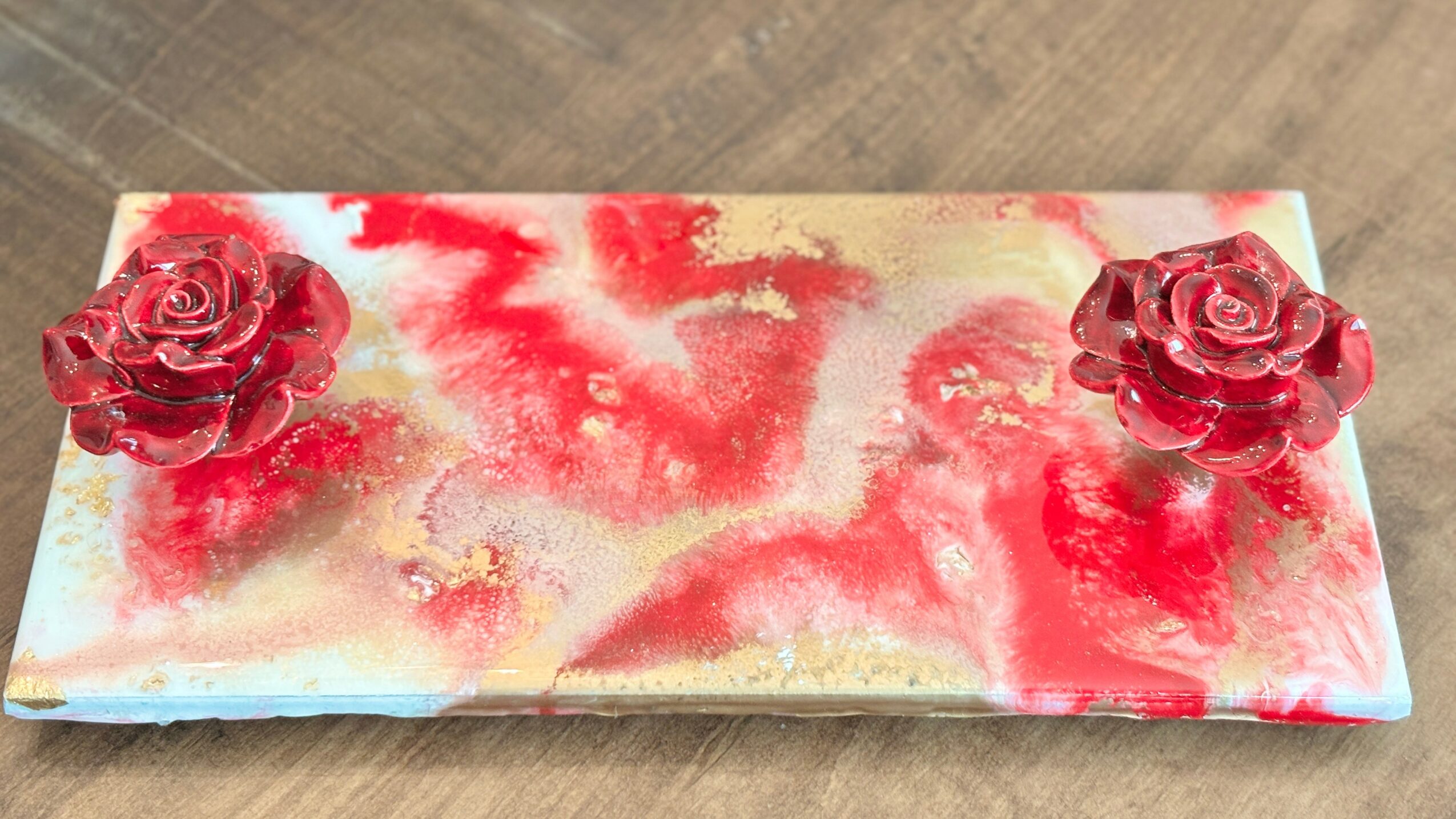 Decorative rectangular tray with two red roses on each end, featuring a red and gold abstract pattern, on a wooden surface.