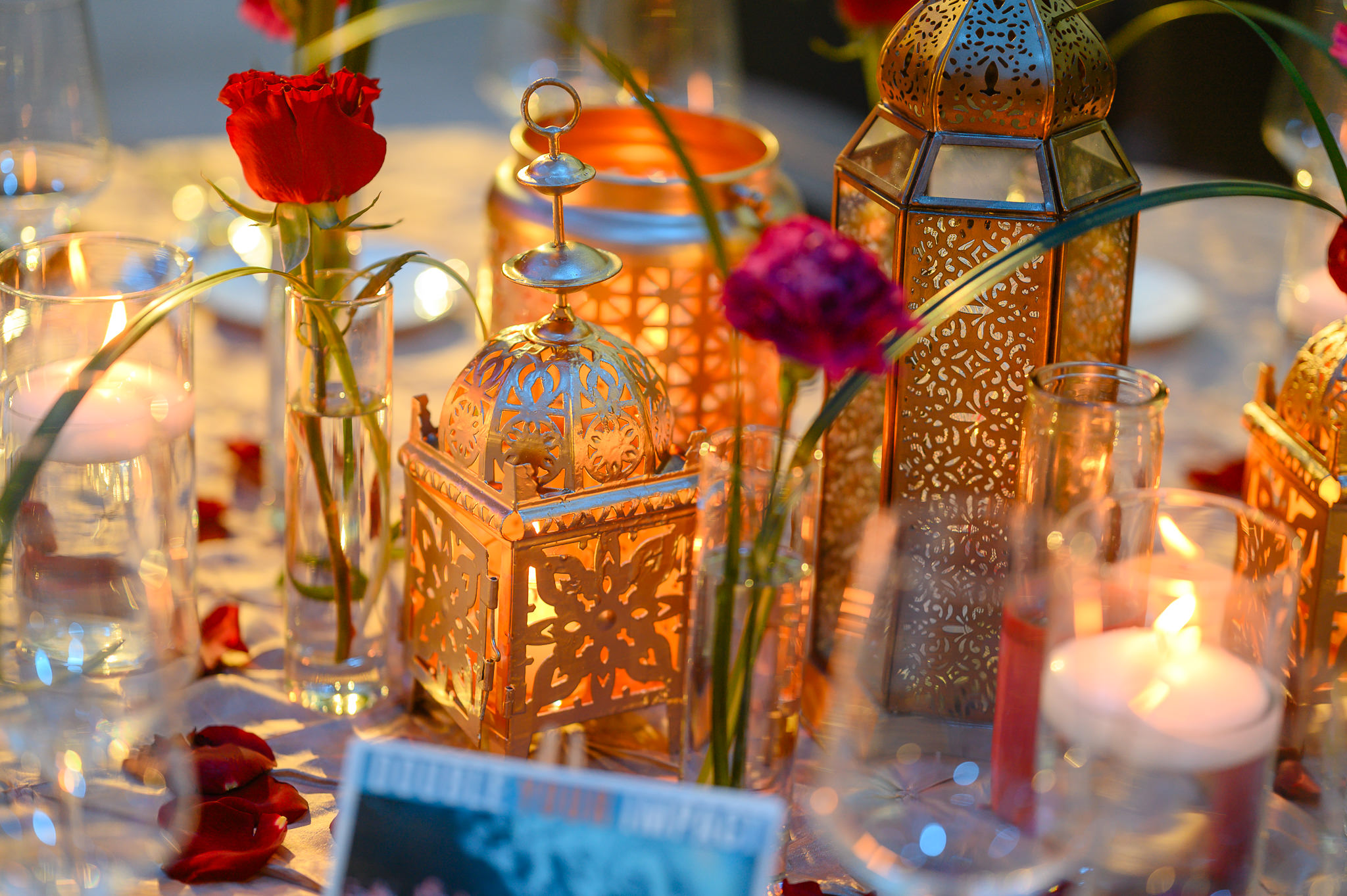 Decorative lanterns, candles, and flowers on a table with warm lighting, creating an elegant setting.
