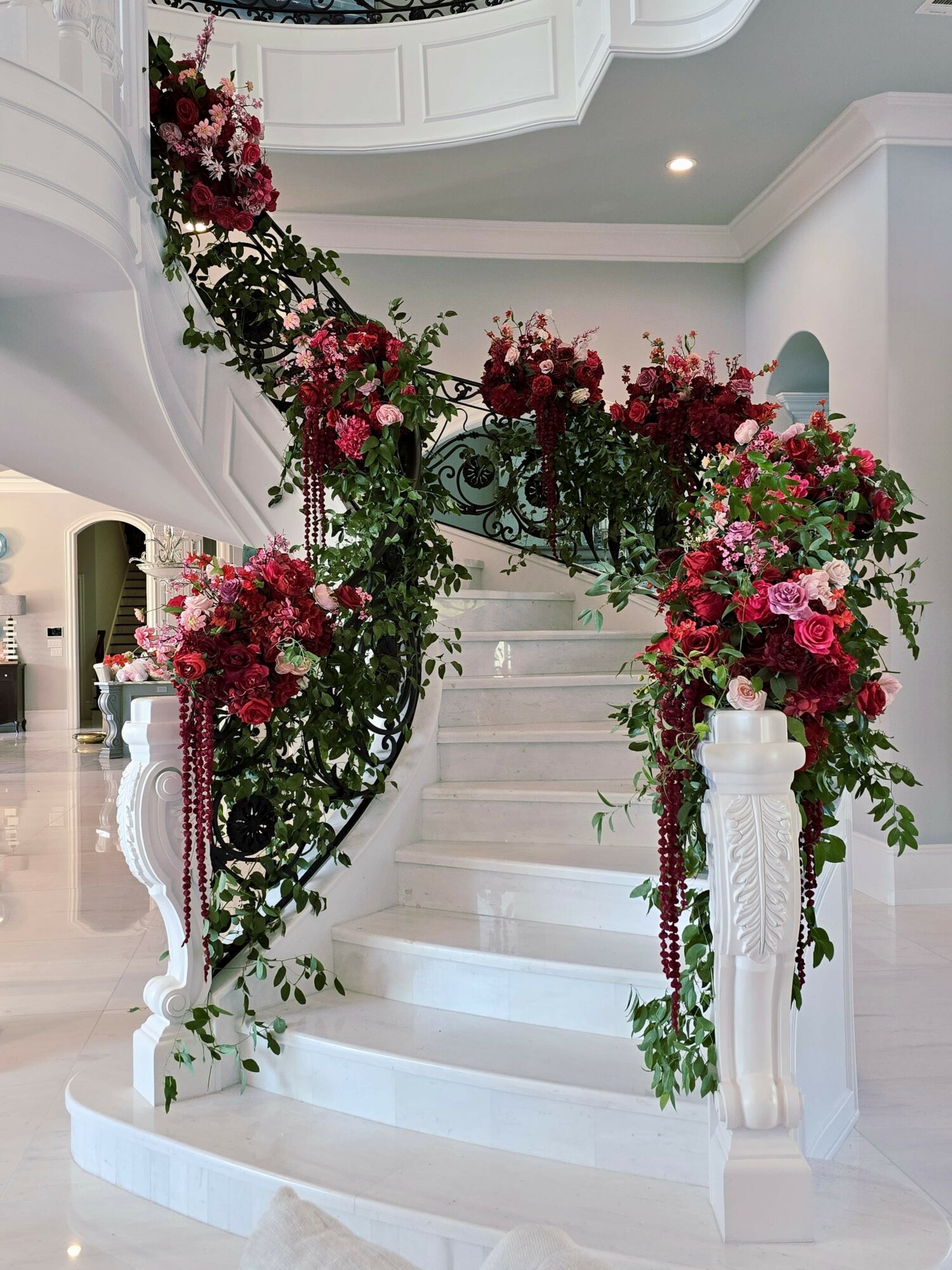 Elegant white staircase decorated with pink and red flowers and greenery, inside a bright, modern home.