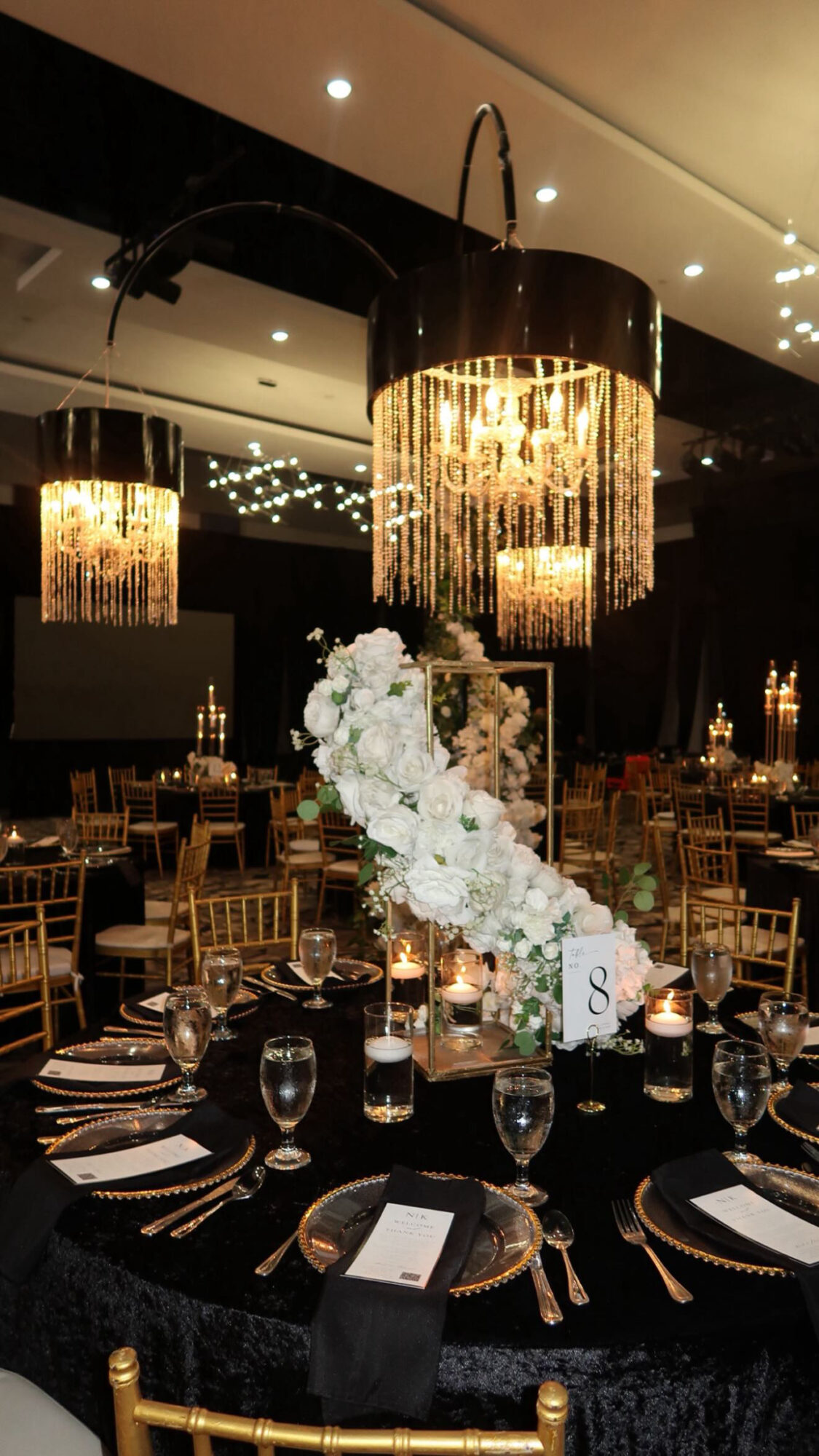 Elegant banquet table with floral centerpiece, candles, and place settings in a decorated event space with chandeliers.
