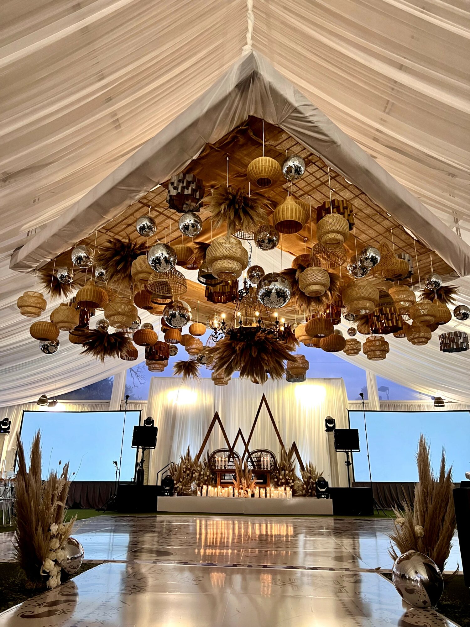 Decorative hanging ornaments and dried plants under a tent ceiling, with a stage and screens in the background.