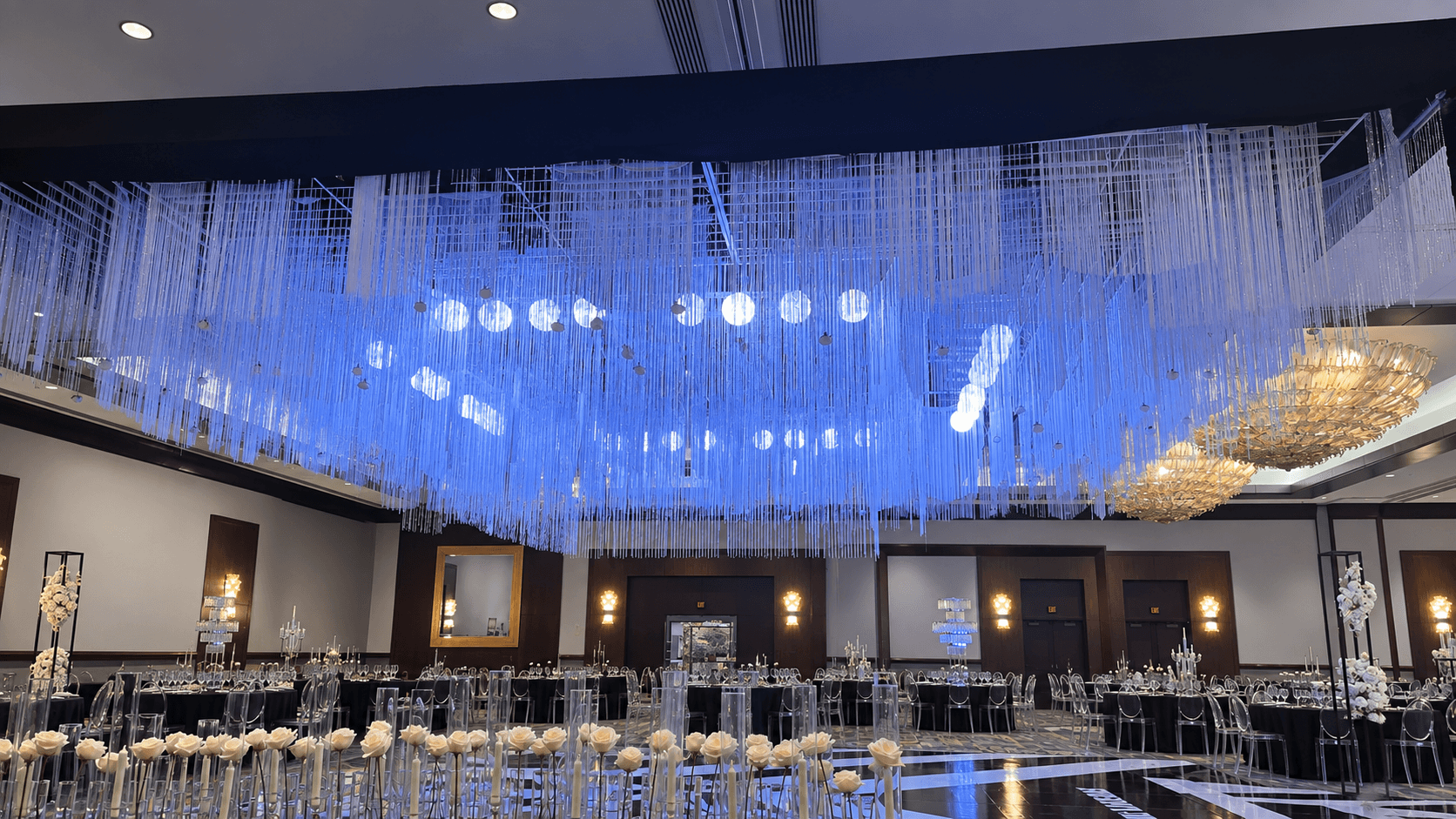 Elegant banquet hall with a large blue chandelier and decorated tables, walls with framed artwork, and ambient lighting.