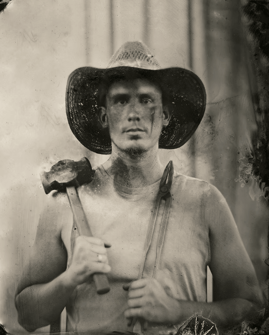 Man wearing a wide-brimmed hat holding a hammer and a pair of pliers, standing outdoors.