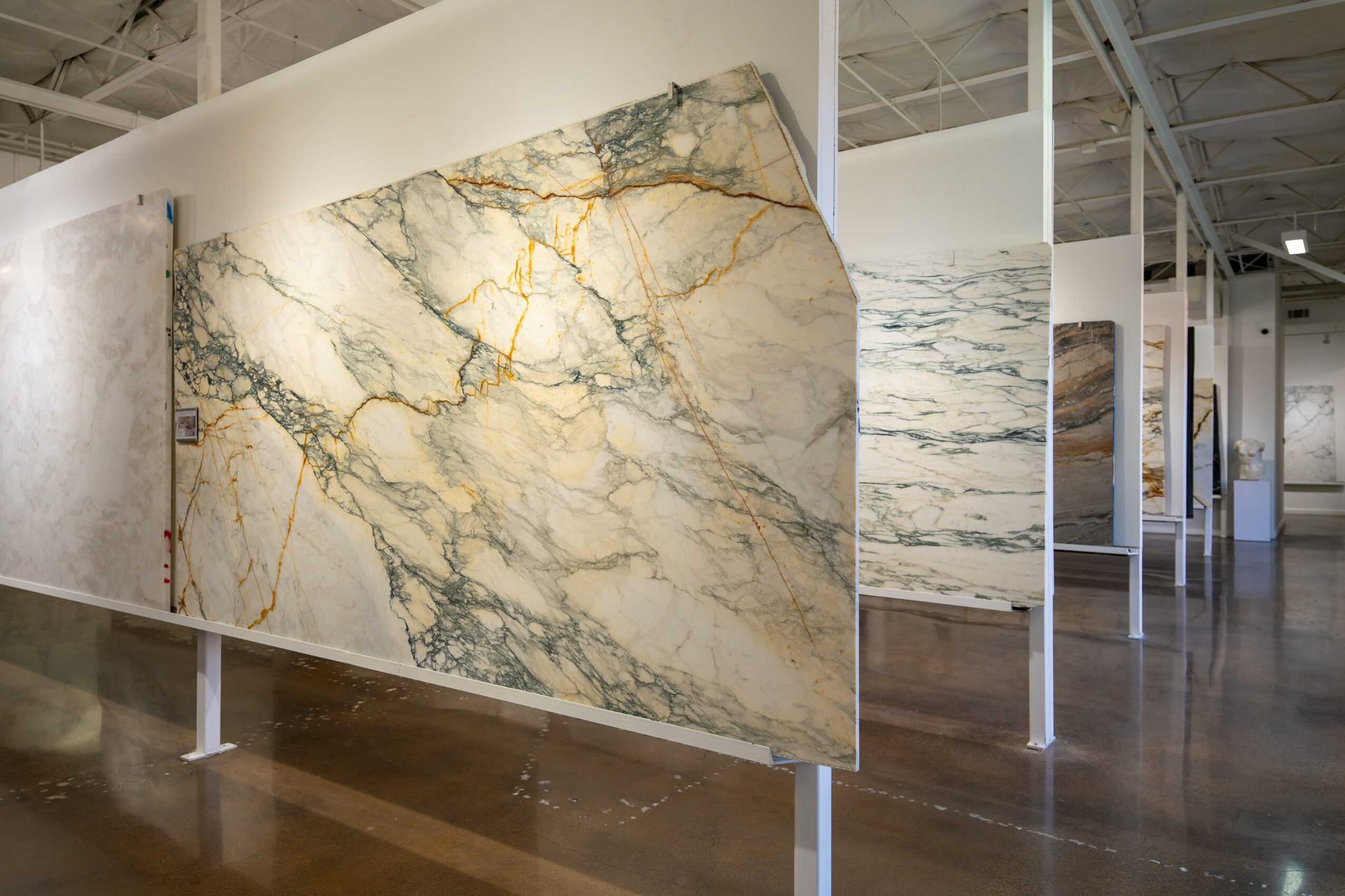 Large marble slab with white, gray, and gold veining displayed in an art gallery or showroom.