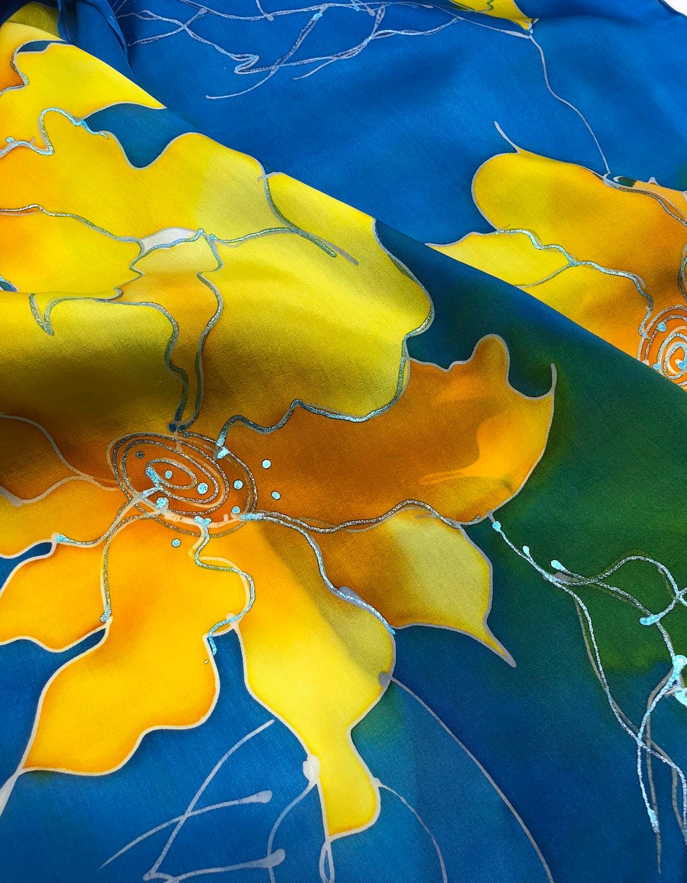 Colorful abstract fabric with yellow, blue, orange, and green sections, outlined with white lines, resembling a floral pattern.
