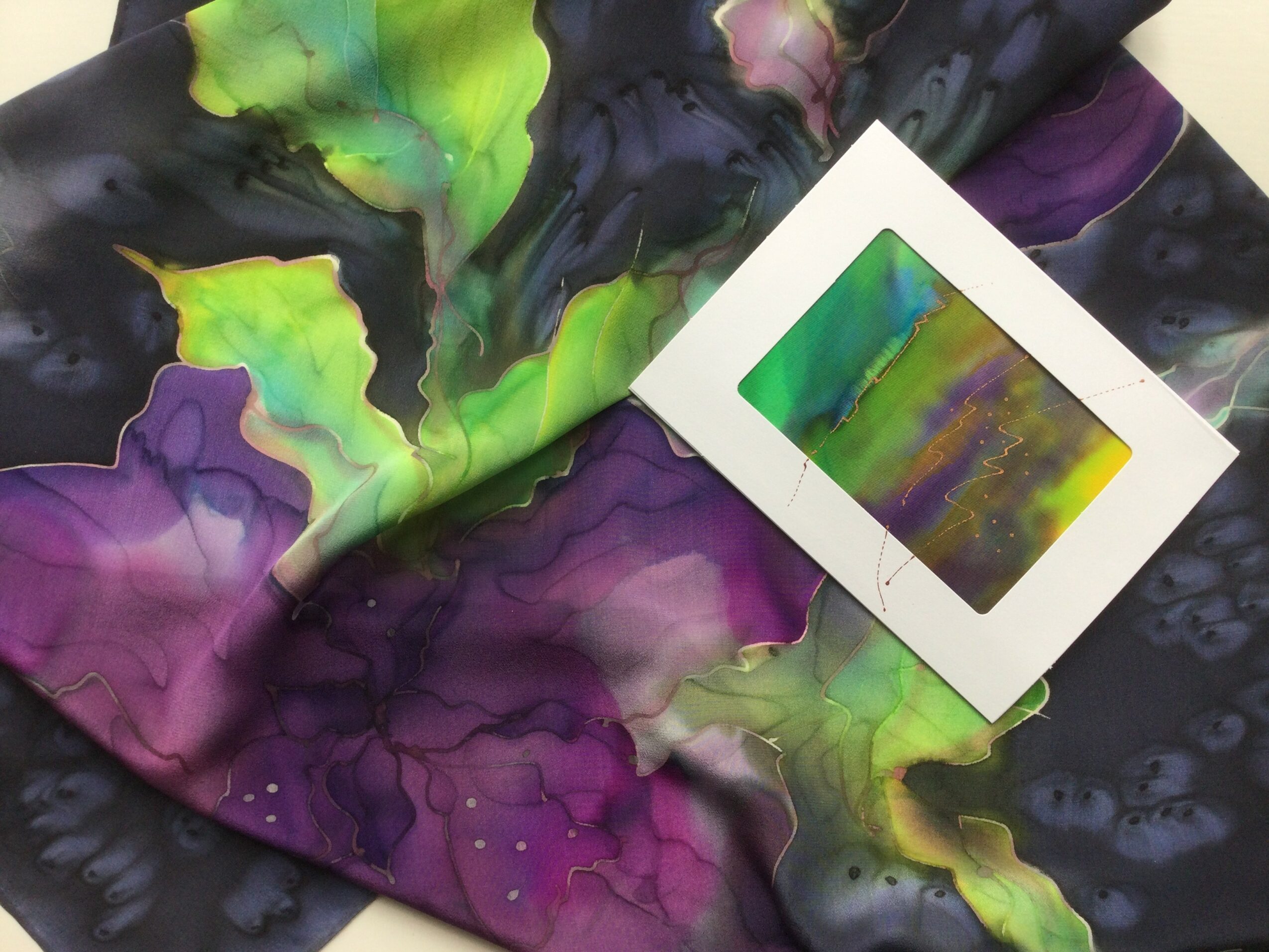 Colorful abstract fabric with green, purple, and yellow hues, and a small framed artwork resting on it.