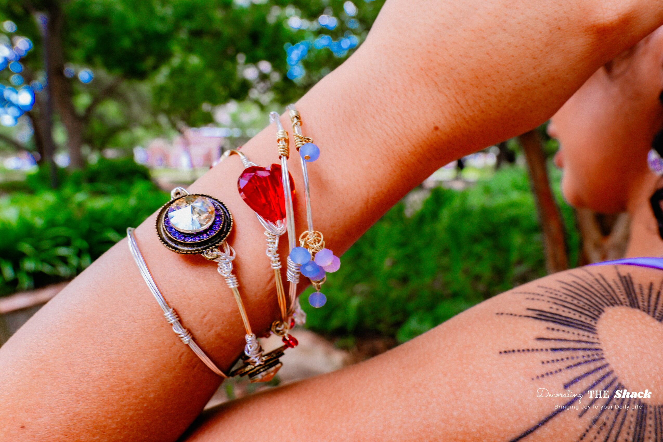 Close-up of a person's wrist with multiple colorful bracelets, outdoors with greenery in the background.