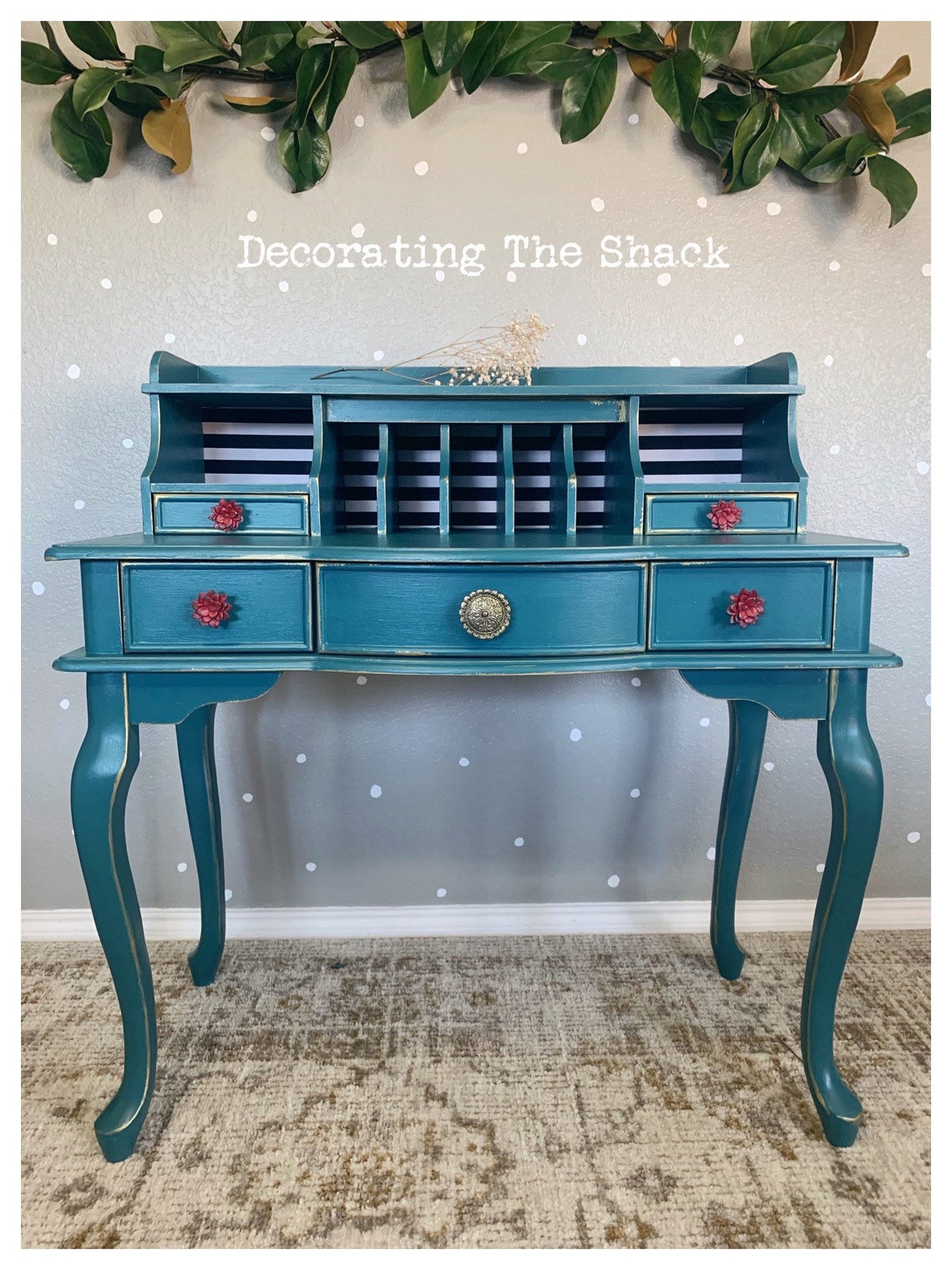 Blue vintage desk with drawers and small compartments, decorated with plants above, on a patterned rug, with text 'Decorating The Snack' above.