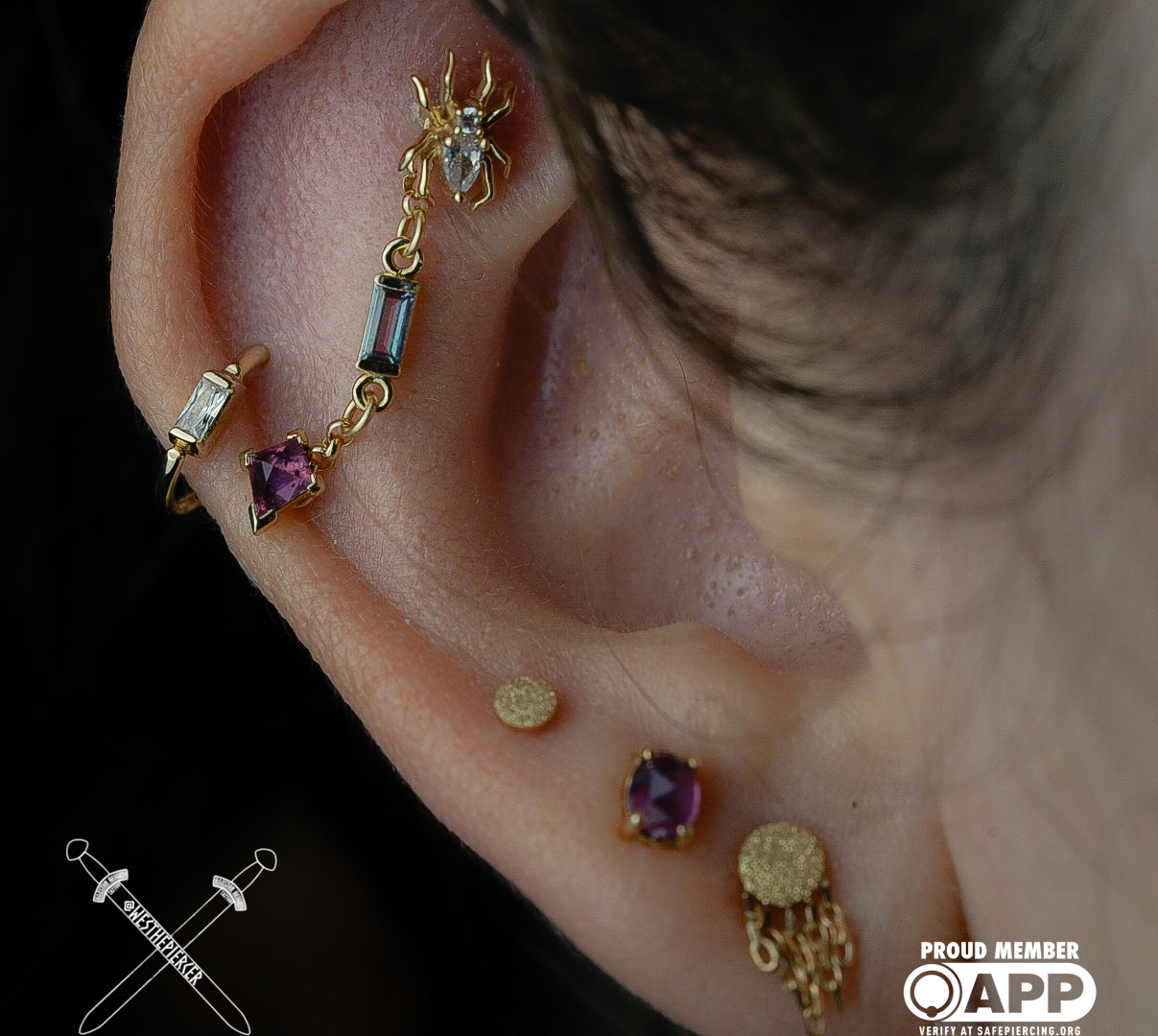 Close-up of a person's ear with multiple earrings, including gold, purple, and gemstone designs.