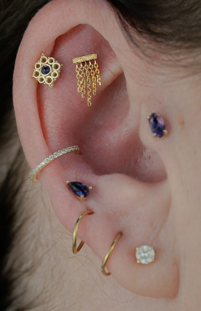 Close-up of a person's ear with multiple earrings, including gold, silver, and gemstone designs.