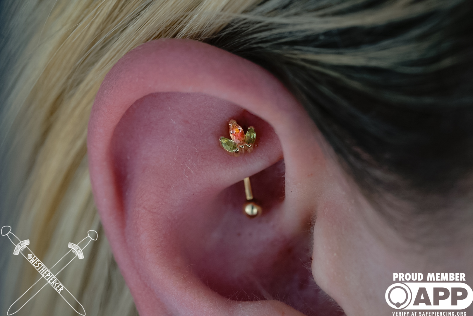 Close-up of a person's ear with two piercings, one with a small flower-shaped earring and the other with a gold ball.