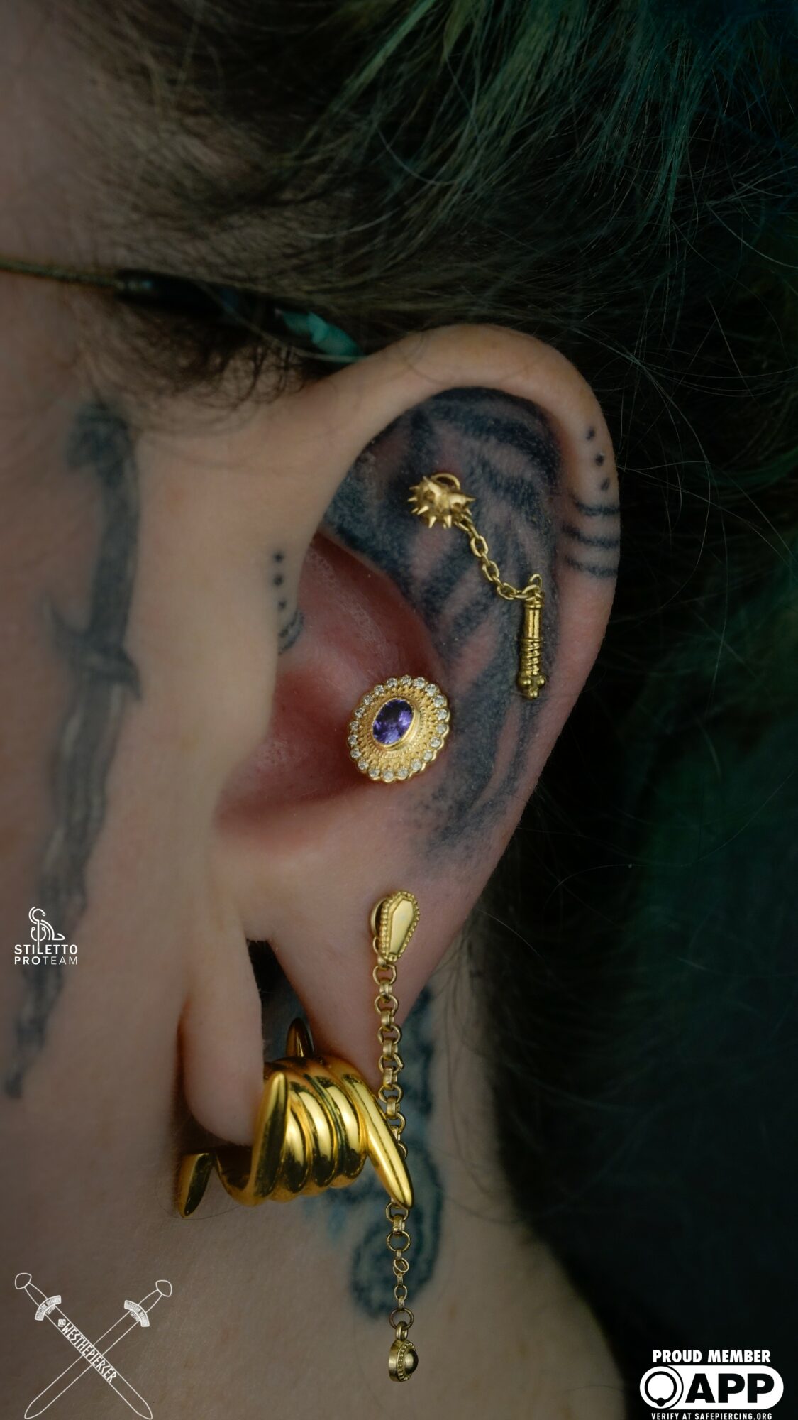 Close-up of a person's ear with multiple gold earrings and a tattoo behind the ear.