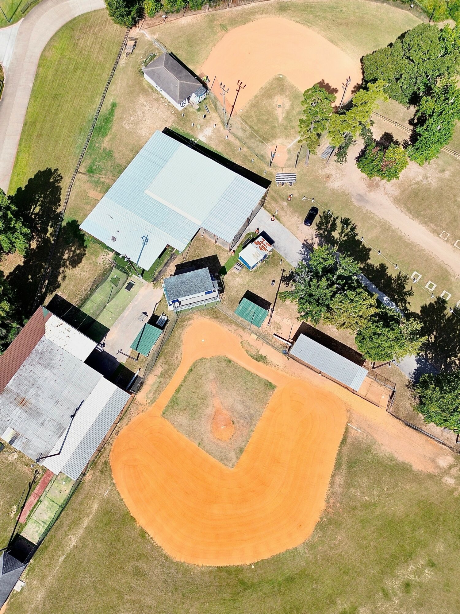 Aerial view of a sports field, baseball diamond, and surrounding buildings with trees and grassy areas.