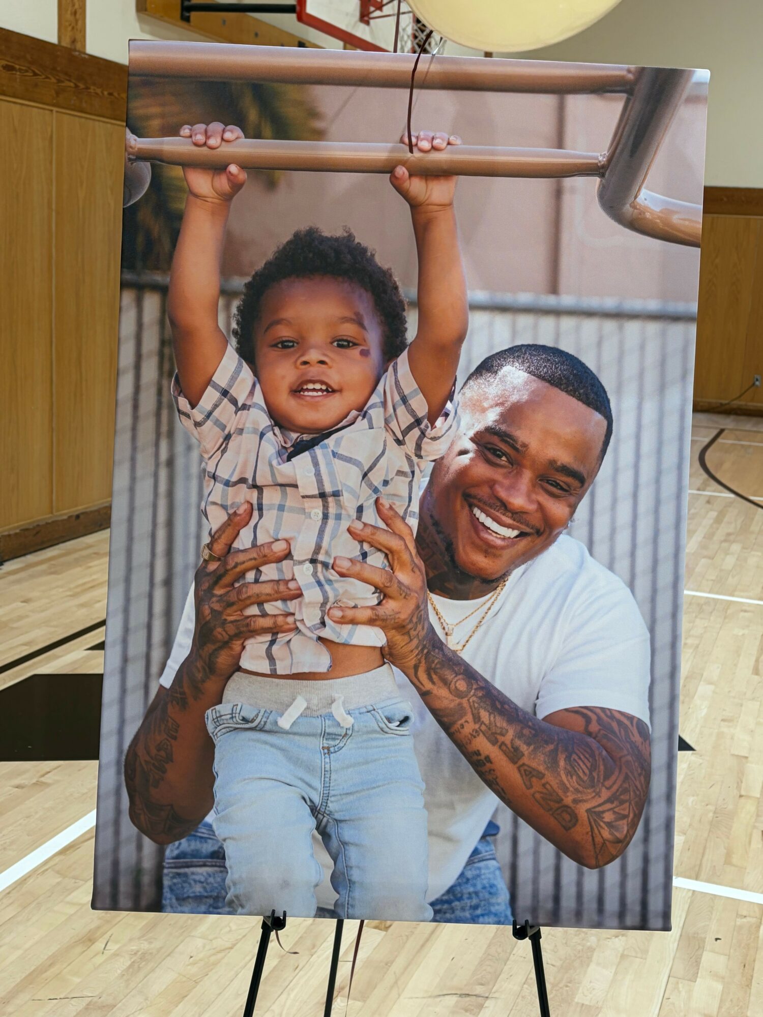 A smiling man with tattoos and a young boy lying on a table, holding a string with a small object, in a room.