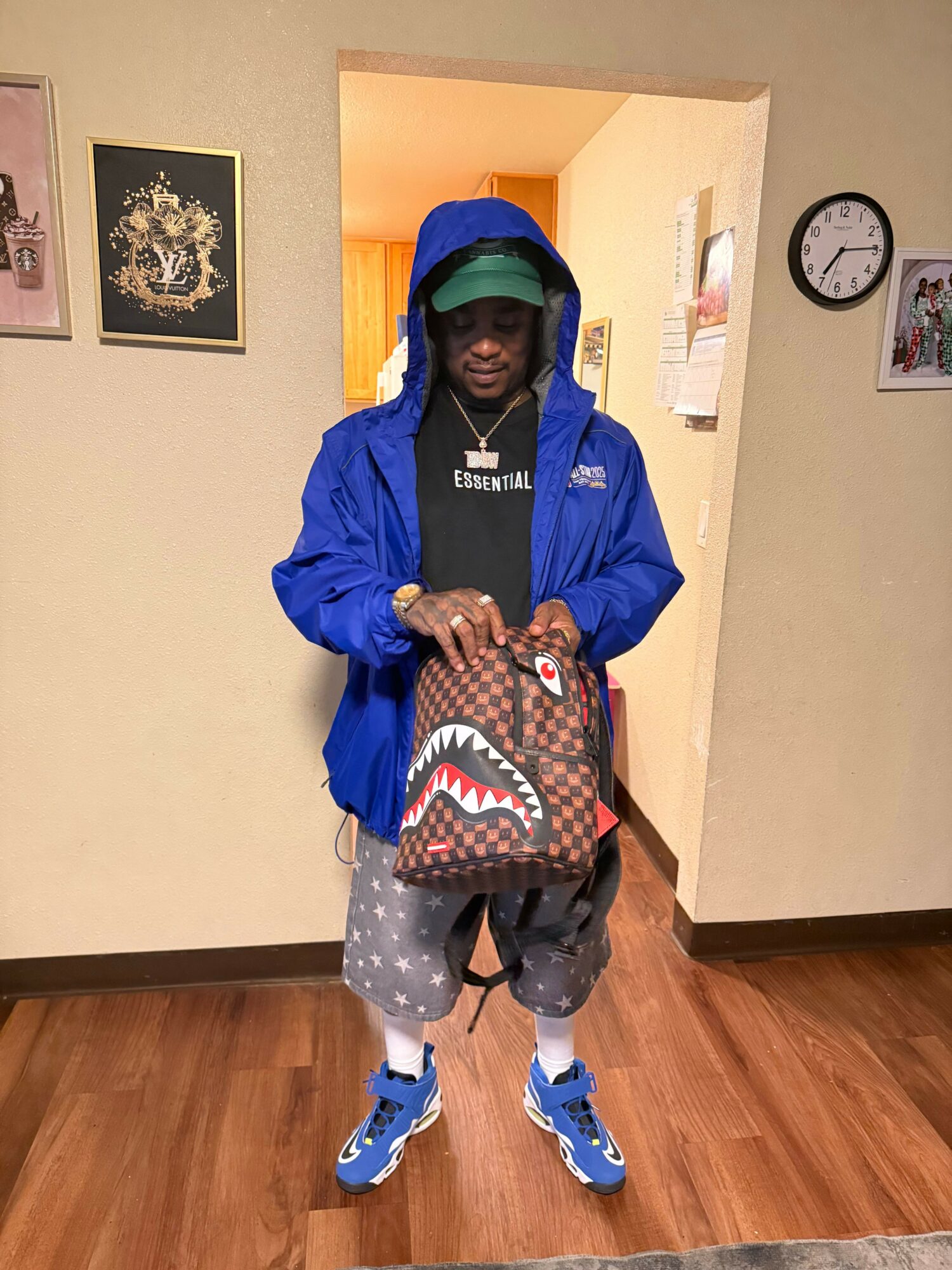 Person taking a mirror selfie in a hallway, holding a bag with a shark mouth design, wearing a blue jacket, gray pants, and blue shoes.