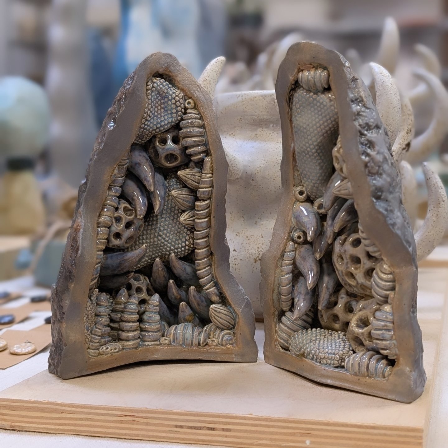 Two clay sculptures filled with various small objects, standing on a wooden surface, with a blurred background.