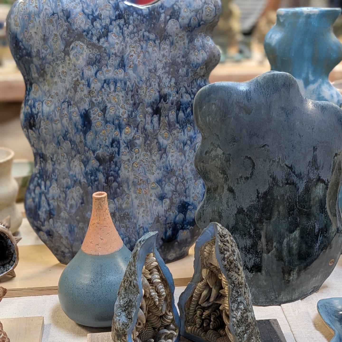 Collection of ceramic vases and sculptures with textured surfaces and blue tones displayed on a table.
