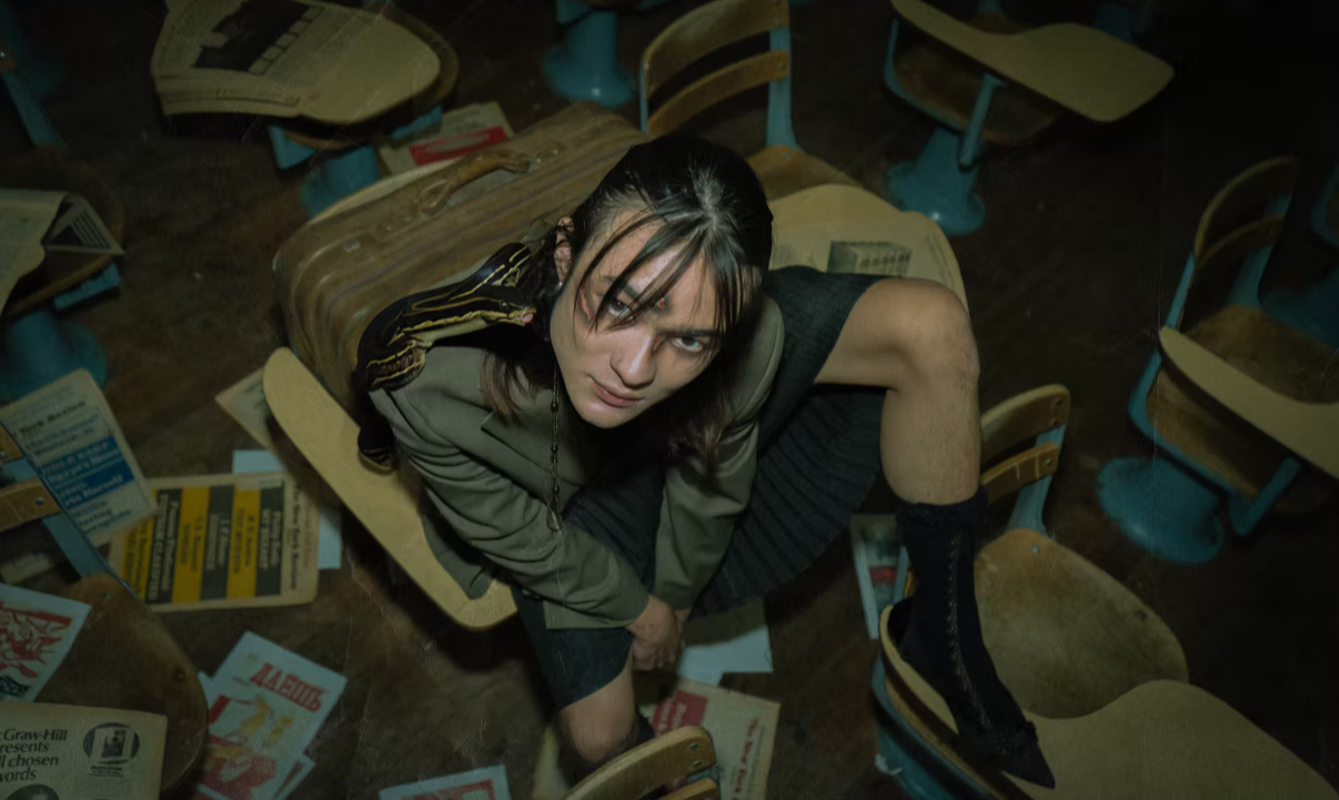 Woman sitting on a chair in a cluttered room with scattered papers and chairs around her.