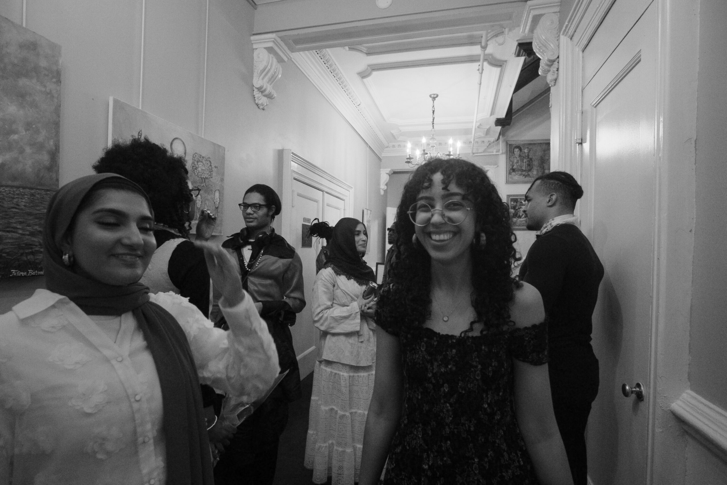 Group of people in a hallway, some smiling and talking, with ornate ceiling and wall details.