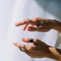 Hands with rings and black nail polish, positioned horizontally, against a light background.