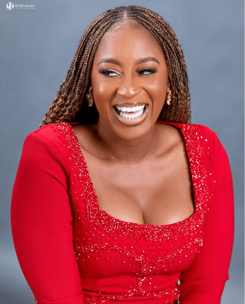 Woman with braided hair smiling, wearing a red dress with embellishments, against a gray background.