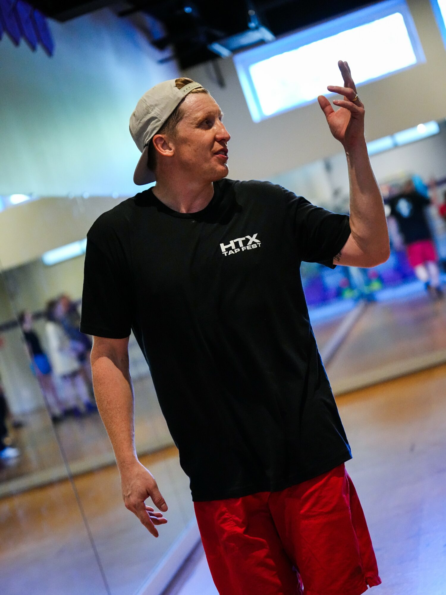 Person wearing a cap and black shirt pointing upward in a gym or dance studio.