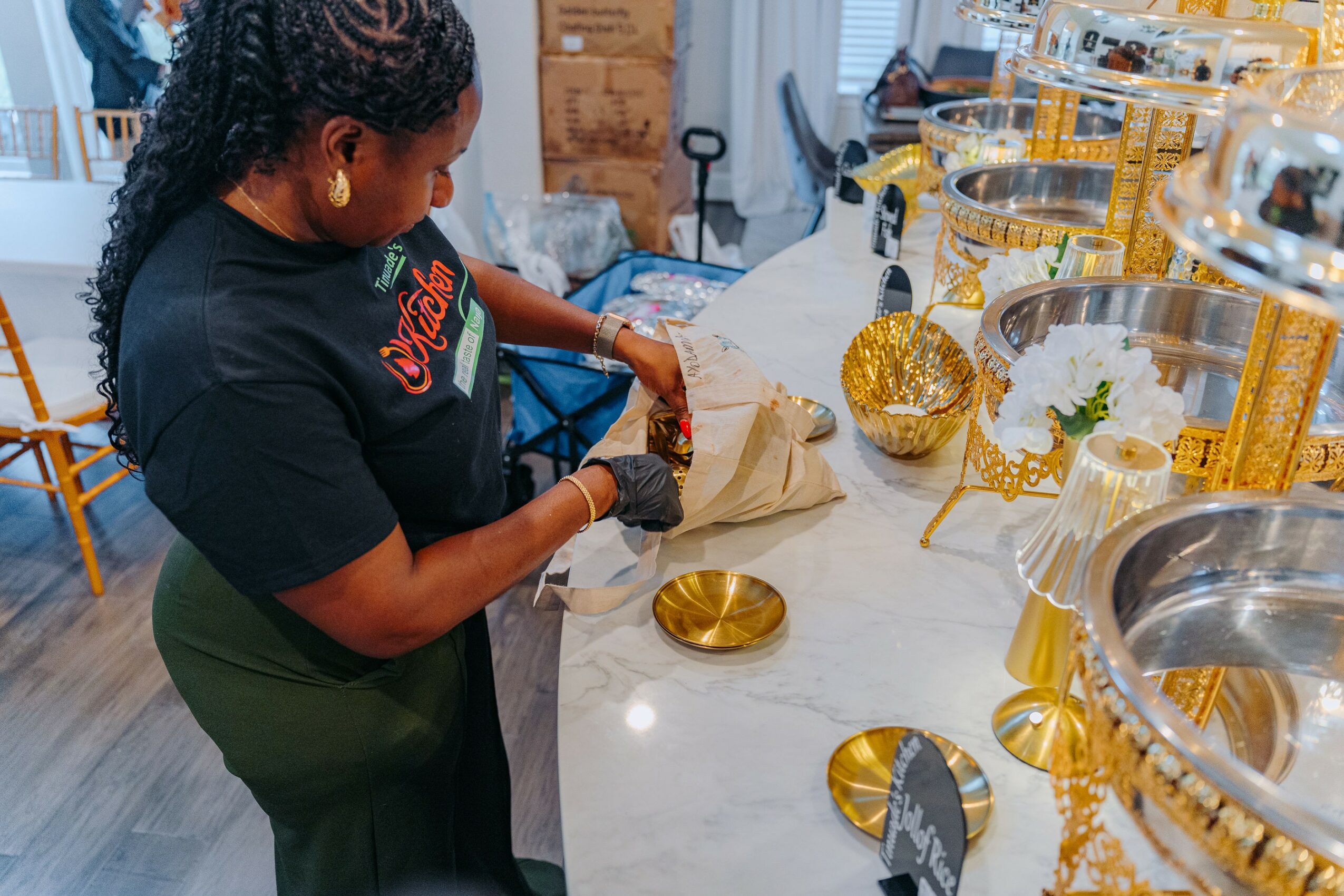 Woman with braided hair wearing a black Coca-Cola shirt, preparing items at a display with gold and silver decorations.